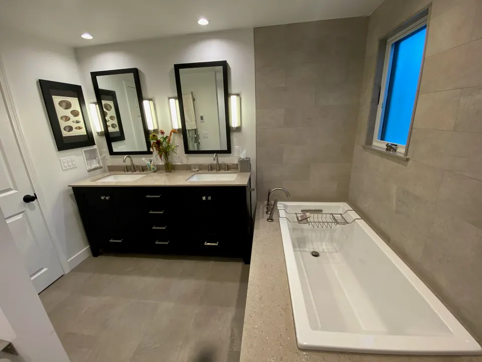 Bathroom with a double vanity, a soaking tub set in a stone deck and a large-format gray tile wall