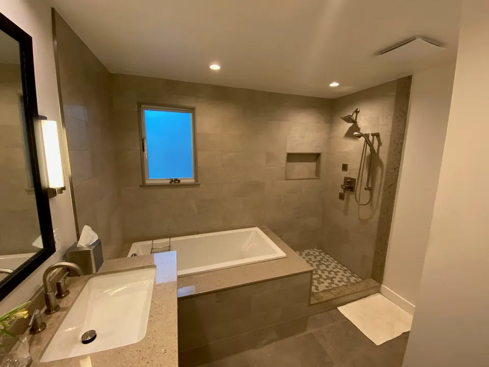 Bathroom with large-format gray porcelain walls, a soaking tub with a tiled apron and a walk-in shower with a niche and mosaic floor