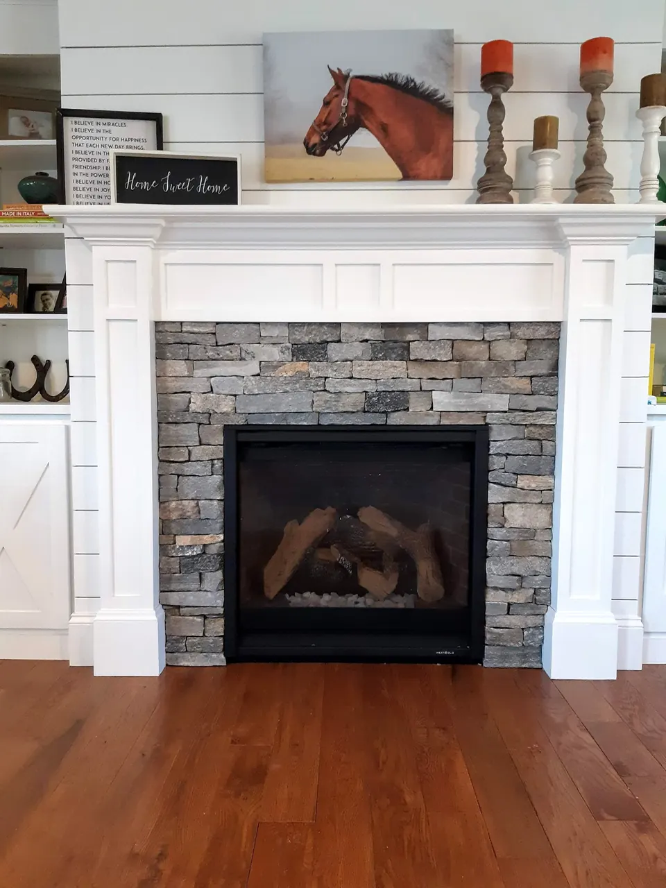 Fireplace surround of gray stacked stone framed by a white mantel and a shiplap wall