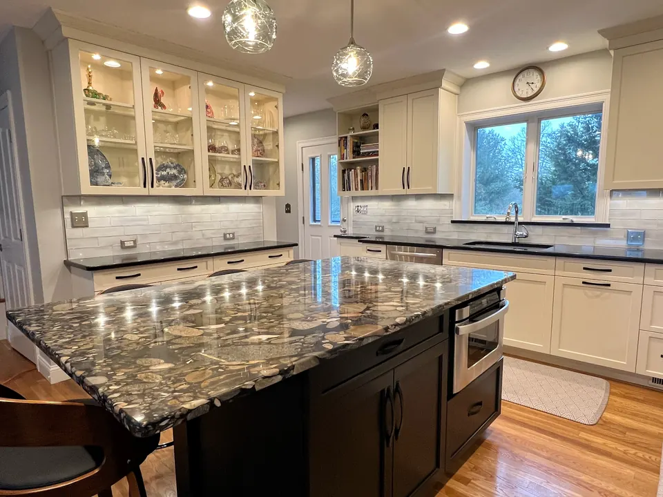 Kitchen with a gray glass subway tile backsplash, glass-front cabinets and a polished stone island under pendant lights