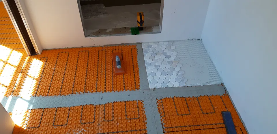 Radiant floor heating cable laid in an orange membrane, with the first white hexagon tiles set in one corner
