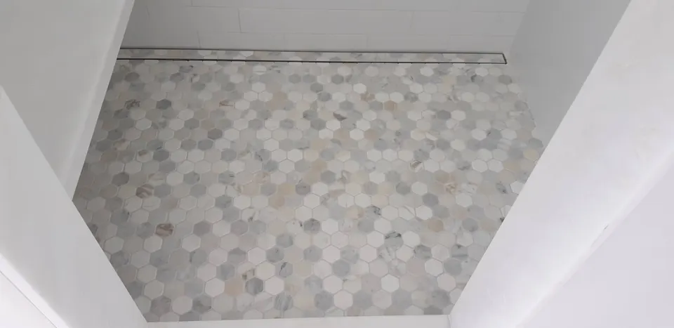 Shower floor of mixed white, gray and beige marble hexagon mosaic with a linear drain along the back wall